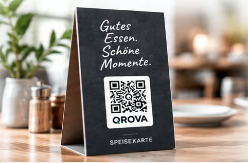 Tischaufsteller mit QROVA-QR-Code auf einem Restauranttisch, daneben Pflanze und Gedeck